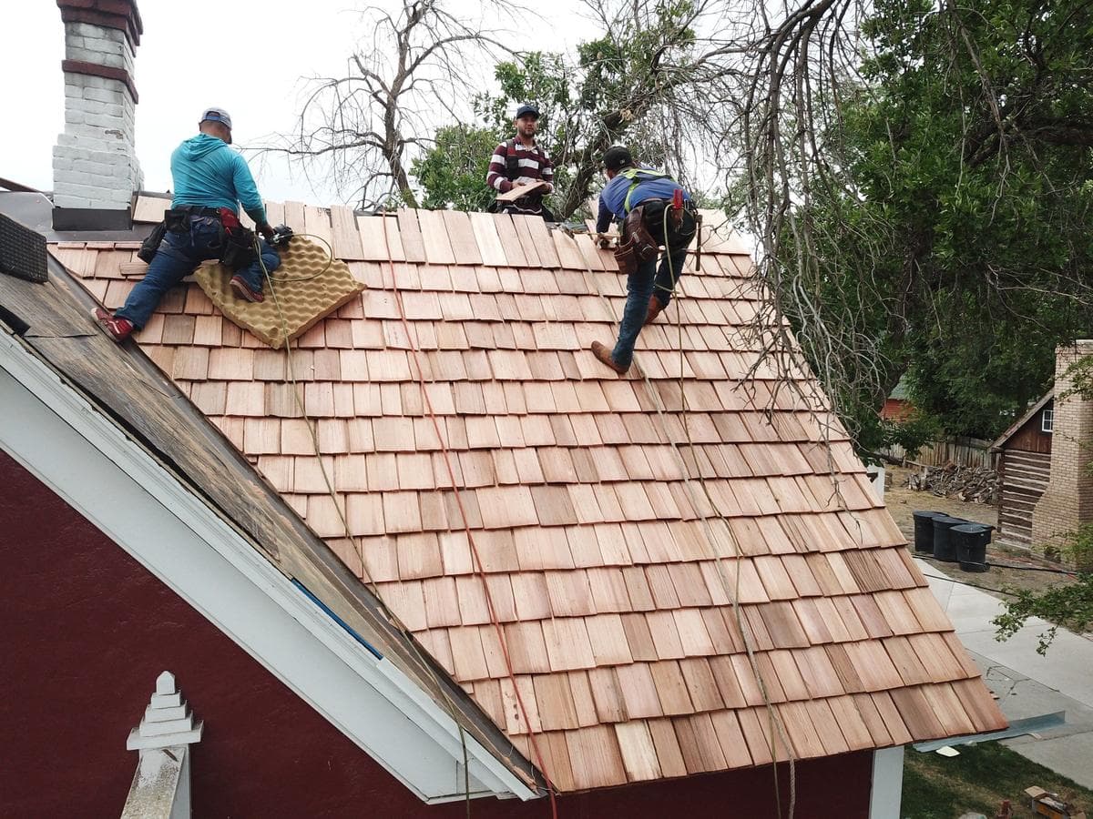 Crew members hand-laying new cedar shake courses on the roof